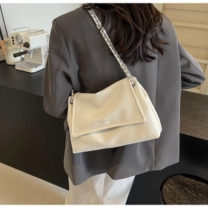 Detail of off-white lychee grain leather crossbody bag with silver chain strap on shoulder