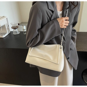 Close-up of white envelope shoulder bag with pleated leather texture and silver chain strap