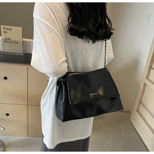 Model wearing a glossy black underarm tote bag with silver chain and white logo