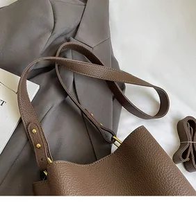 Detail of brown lychee grain leather bucket bag with wide strap and gold metal studs