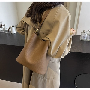 Detail of a brown leather bucket bag with embossed logo and adjustable shoulder strap