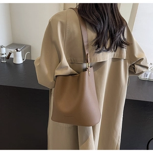 Brown lychee leather bucket bag with pleated design worn by a model in casual setting