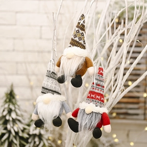 Close-up of three knitted Christmas gnomes hanging on branches with festive lights