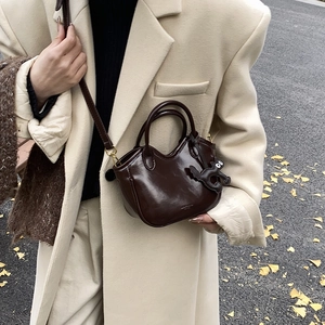 Dark brown oil wax leather bucket bag with cat charm on a scenic autumn street