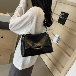 Minimalist black wrinkled leather shoulder bag with silver chain strap worn by a model