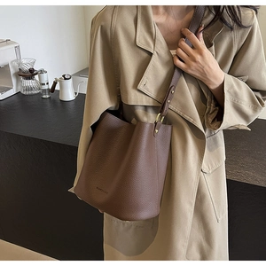 Detail of dark brown pebble leather bucket bag featuring elegant side wear on a trench coat