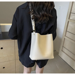 Detail showing white bucket bag with pebble leather texture and golden metal strap buckle