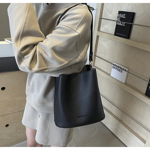 Detail of black lychee grain leather bucket bag with FASHION & BAGS logo and strap
