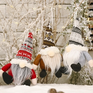 Three Christmas gnome ornaments with knitted hats and beards hanging on snowy branches