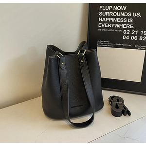 Detail of black lychee grain leather bucket bag with gold hardware on marble surface