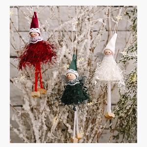Close-up of plush Christmas angel ornaments with sequin wings hanging on snowy branches
