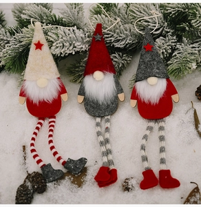 Three plush Christmas forest gnomes with long legs hanging on snowy pine needles