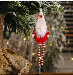 Close-up of a Christmas gnome with striped long legs hanging on a snowy pine branch
