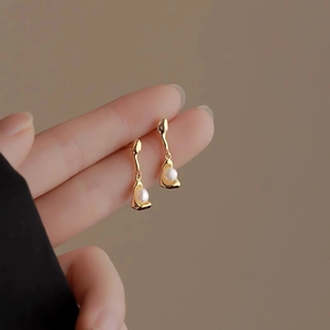 Close-up of irregular gold liquid metal earrings with elegant white pearl drops