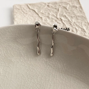 Silver heart earrings with irregular wavy drop pendants on a ceramic bowl