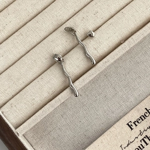 Minimalist silver irregular wavy earrings in polished metal on a beige jewelry display