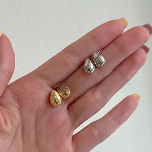 Détail de boucles d'oreilles goutte en or et argent tenues en main pour voir la taille