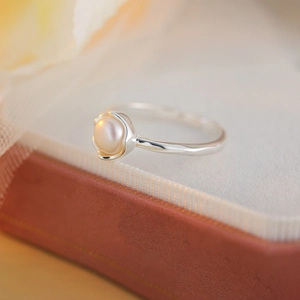 Macro shot of silver pearl ring on a jewelry box edge featuring petal-shaped metal setting