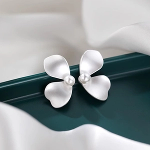 Macro shot of silver matte flower earrings with pearl center on green velvet and satin