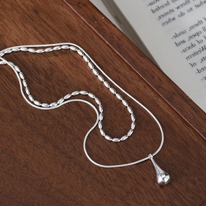 Close-up of double-layered silver necklace with water drop pendant on wooden tray
