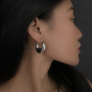 Minimalist silver oval drop hoop earrings with polished metallic finish on model