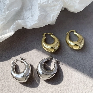 Polished chunky teardrop hoop earrings in gold and silver finishes on a grey textured base