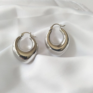 Polished silver teardrop hoop earrings on white silk fabric with a minimalist metal design