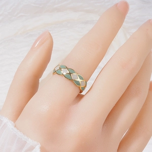Gold French lattice ring with green and white enamel on a white fabric background