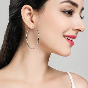Close-up of model wearing large S925 silver geometric diamond-cut hoop earrings