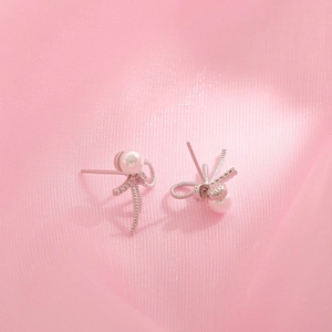 Elegant S925 silver bow stud earrings with pearls and micro-diamonds on pink silk fabric