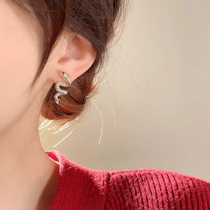 Detailed close-up of golden snake stud earrings with sparkling crystals on earlobe