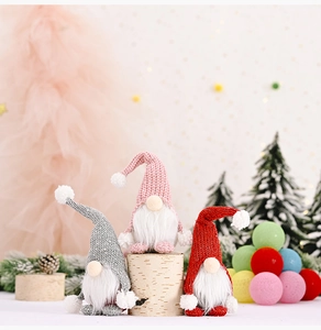 Drei gestrickte Weihnachtswichtel mit weißen Bärten auf einem rustikalen Holzsockel