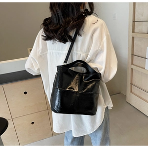 Classic black high-gloss bucket bag with adjustable shoulder strap on a model back