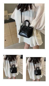 Close-up of black glossy leather bucket bag with silver sphere charm and brand lettering