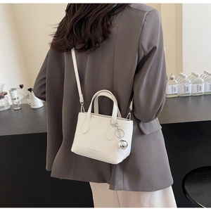 Detail of white leather bucket bag featuring silver ball charm and long shoulder strap