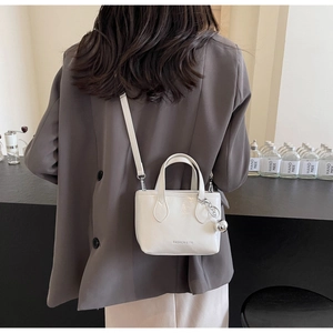 Detail of a white mini patent leather bucket bag with silver ball charm and shoulder strap