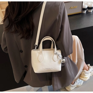 Detail of cream white leather bucket bag with silver ball charm and crossbody strap