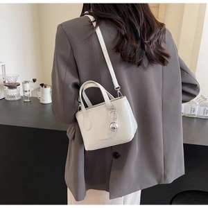 Detail of a white mini bucket bag with silver metal ball charm on a grey suit model