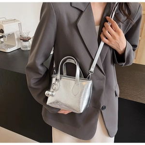 Detail of silver metallic bucket bag with FASHION & YM logo and sphere charm