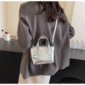 Silver metallic mini bucket bag with spherical charm and long strap shown on model back