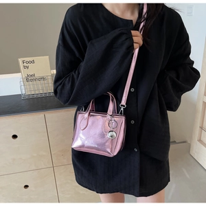 Detail of pink metallic bucket bag with dual handles and silver ball pendant accessory