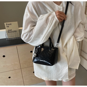 Detail of black glossy patent leather bucket bag with silver ball charm and shoulder strap