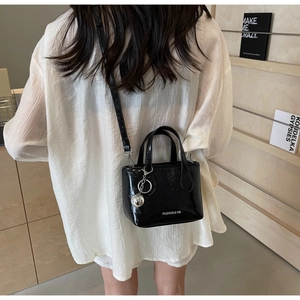 Detail of glossy black leather bucket bag with silver ball charm shown in casual setting