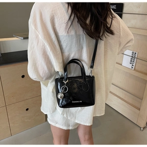 Detail of black glossy leather bucket bag with silver ball charm and brand logo