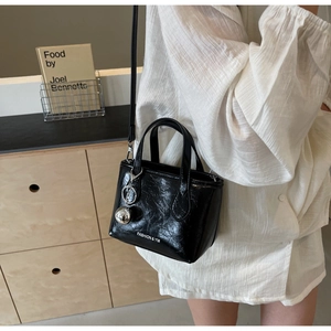 Detail of black glossy wrinkled texture handbag with silver ball charm and brand logo