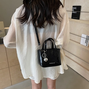 Minimalist black glossy bucket bag with wrinkled texture and silver ball charm