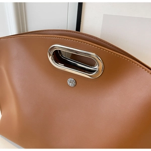 Detail of a brown leather bag showing the oval metal handle and magnetic honeycomb clasp