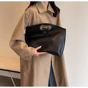 Macro shot of minimalist black leather tote bag with silver metal handle on beige trench coat