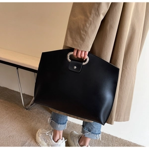 Close-up of black tote bag with silver circular metal handle and snap closure detail