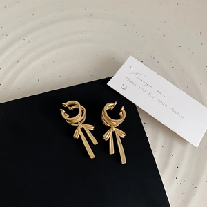 Detail of matte gold bow ear cuff earrings with triple rings and ribbon tassel drops